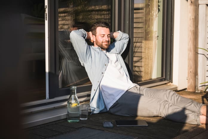 Smiling freelancer with hands behind head relaxing on porch