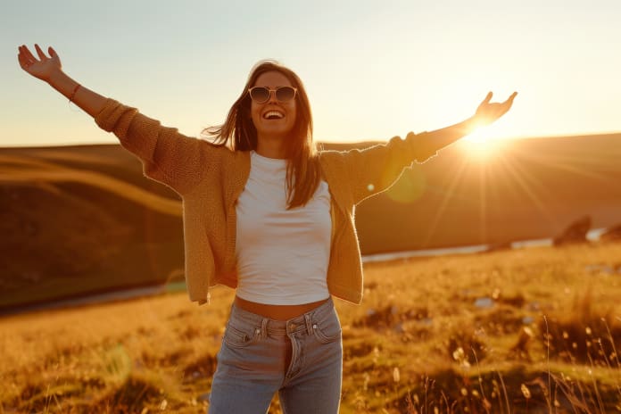 A joyful woman enjoys the sunset over a serene landscape with outstretched arms in a golden field