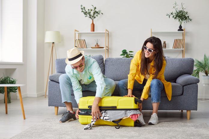 Portrait of a young happy couple packing suitcase for vacation trip at home together.